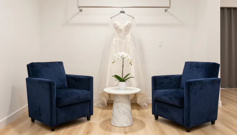 Concept visual: a customer waiting area with two navy armchairs, a marble table and a gown displayed on a rail