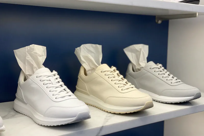 Illustration: three pairs of freshly cleaned sneakers wrapped in tissue on a marble shelf against a navy wall
